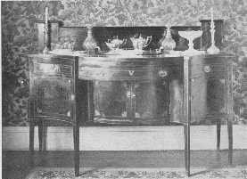 A fine old Hepplewhite sideboard, with old glass and
 silver, but the modern wallpaper is not in harmony.