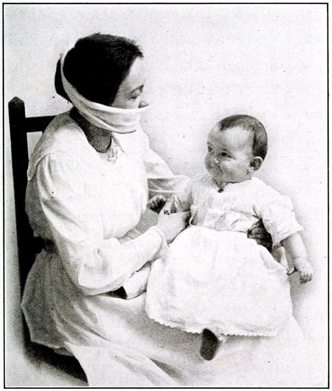 A woman wearing a mask covering their
mouth and nose while holding a baby